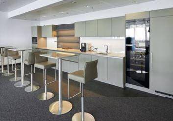 Moderne Büroküche mit minimalistischen Schränken, integrierten Geräten und Stehtischen für Pausen.