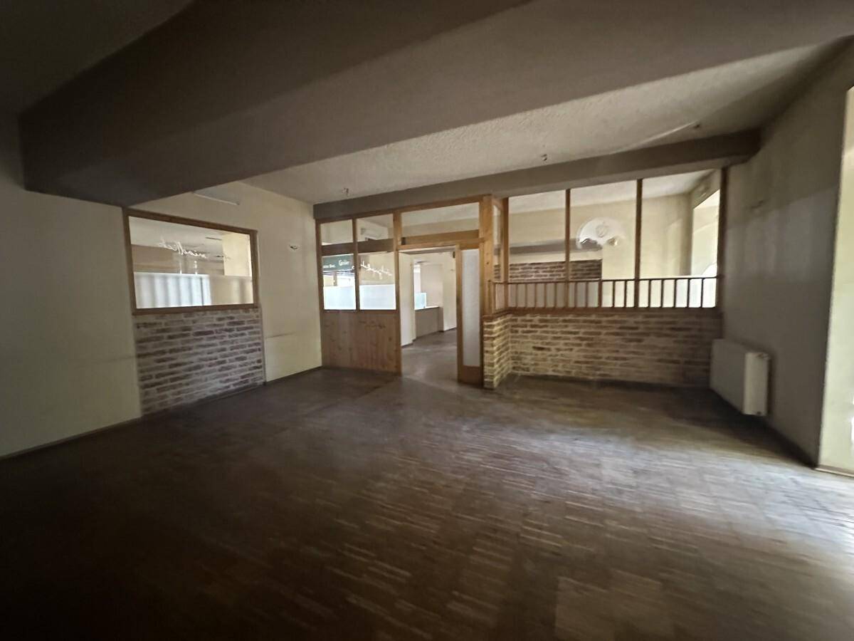 Großer Gewerberaum mit Holzboden, Ziegelwänden und einem Durchgang zu weiteren Bereichen.