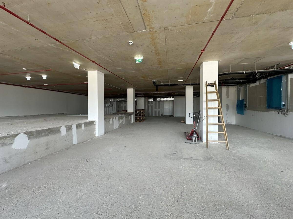 Großer, unfertiger Gewerberaum mit Betonboden und -decke, weißen Säulen und sichtbaren Installationen.