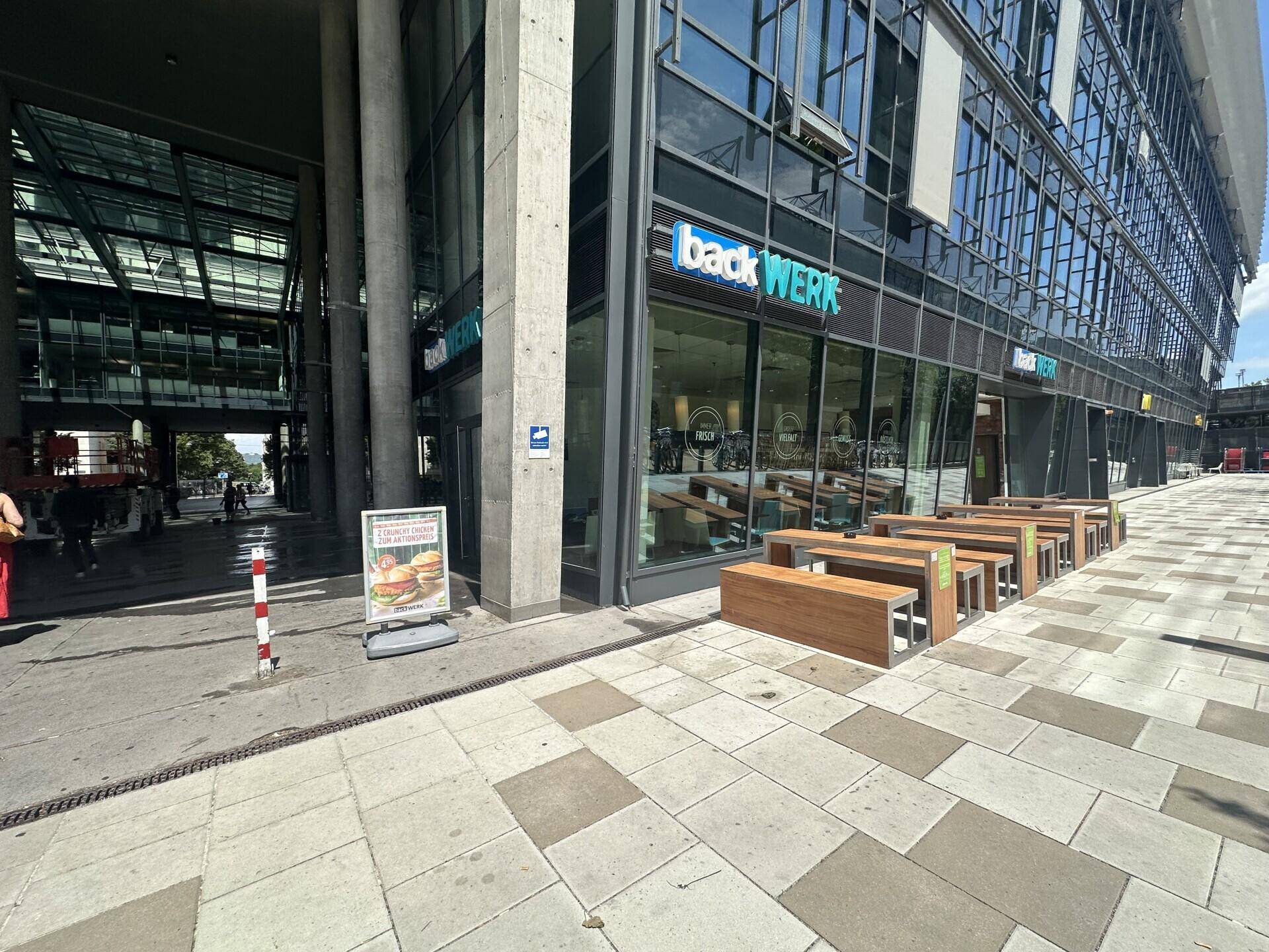 Außenansicht eines modernen Geschäftsgebäudes mit großen Fenstern und Sitzbänken auf dem Bürgersteig.