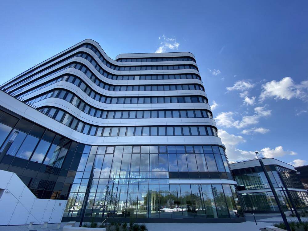 Detailansicht der geschwungenen Glasfassade eines modernen Bürogebäudes unter klarem Himmel.
