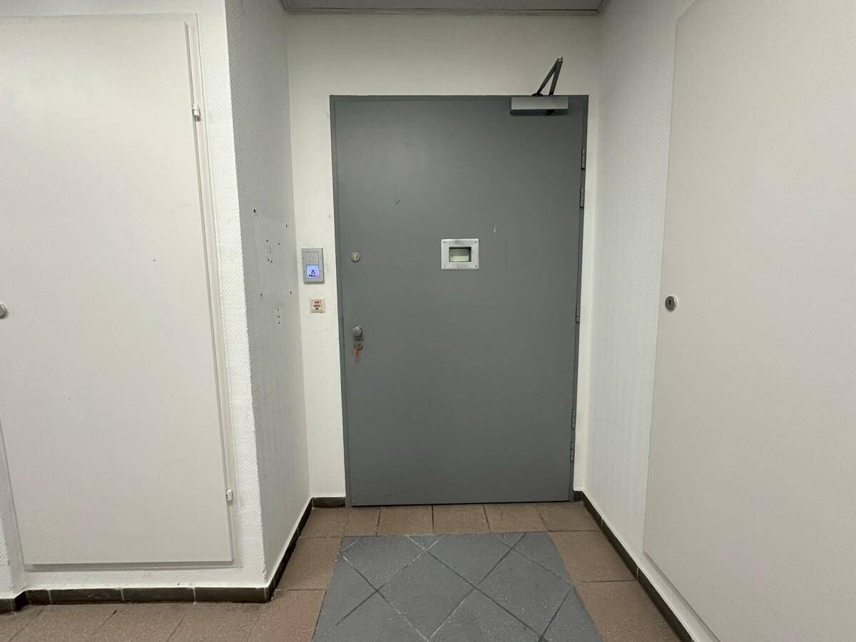 Eingangsbereich mit einer robusten grauen Tür und Fliesenboden, umgeben von weißen Wänden.