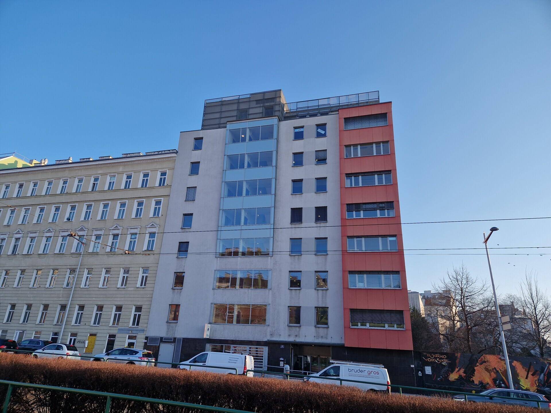 Zeitgenössisches Bürogebäude mit großen Fenstern und klaren Linien an einer belebten Straße.