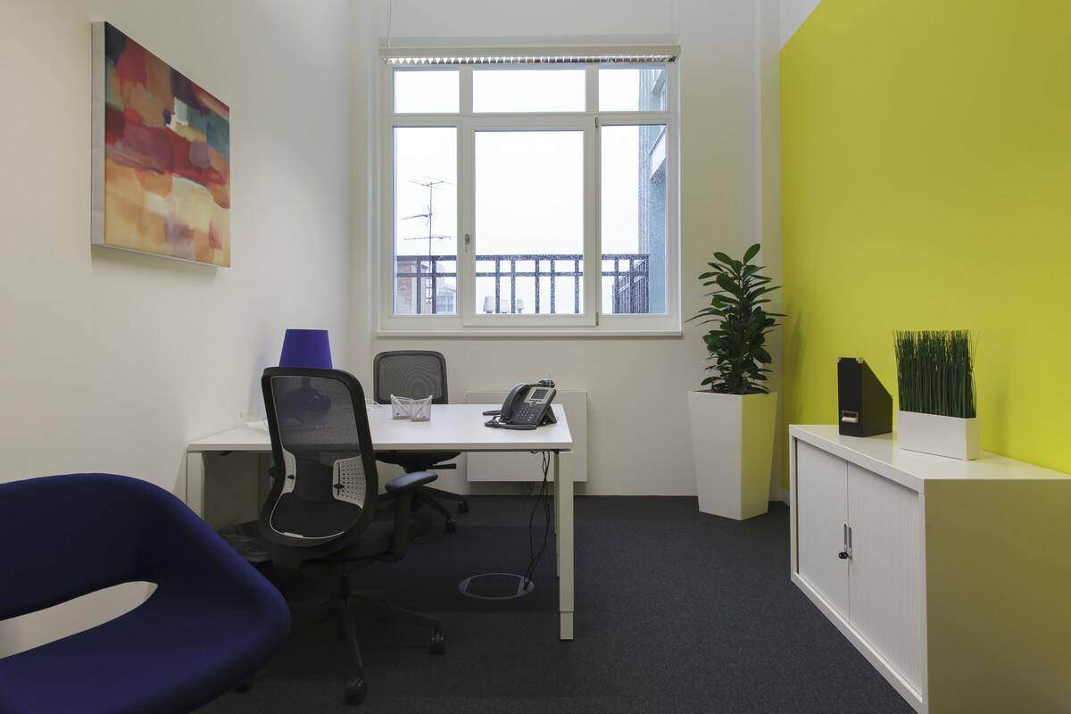 Helles Einzelbüro mit einem großen Fenster, einem Schreibtisch und einem Farbakzent an der Wand für eine lebendige Atmosphäre.