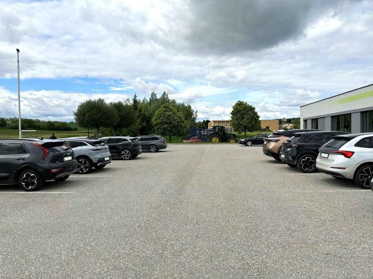 Großer Parkplatz mit mehreren Autos und Blick auf eine ländliche Umgebung mit Bäumen und Feldern.