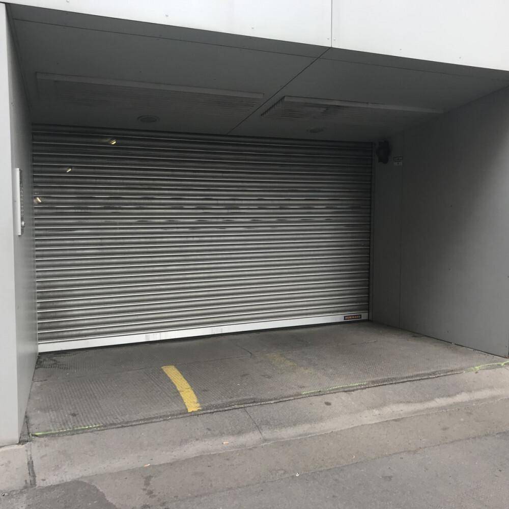Einfahrt zu einer Tiefgarage mit geschlossenem Rolltor und einer gelben Markierung auf dem Boden.