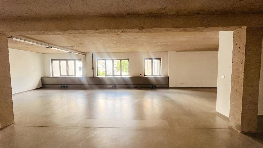 Heller, offener Büroraum mit mehreren Fenstern, die viel Sonnenlicht hereinlassen, und einem robusten Betonboden.