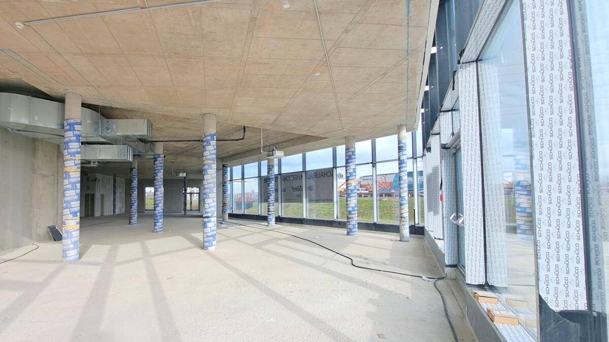 Innenansicht des Rohbaus mit geschwungener Glasfassade, Betonboden und sichtbaren Säulen.