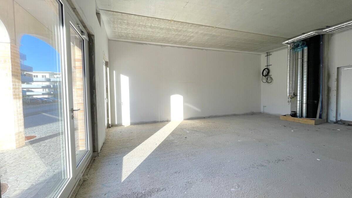 Heller Gewerberaum im Rohbau mit Betonboden, großen Fenstern und viel natürlichem Lichteinfall.