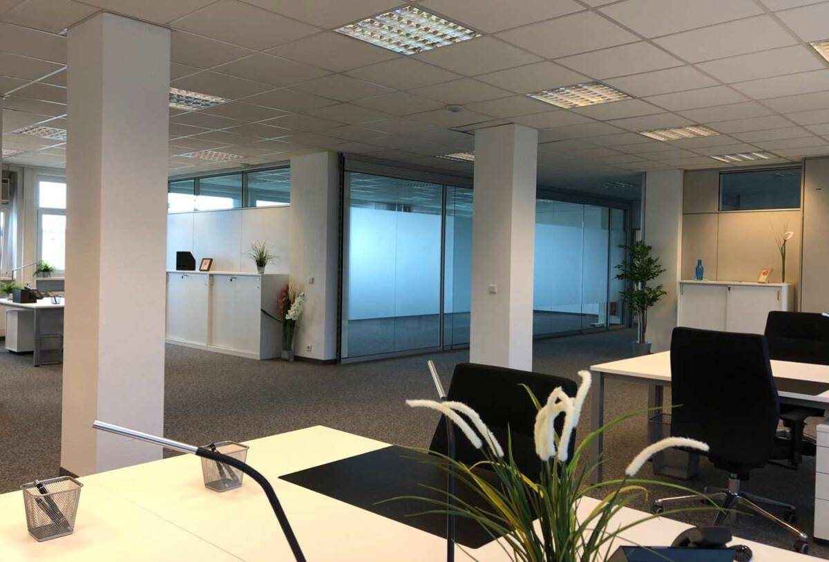 Großzügiger Büroraum mit Teppichboden, Säulen und modernen Glasabtrennungen für separate Arbeitsbereiche.
