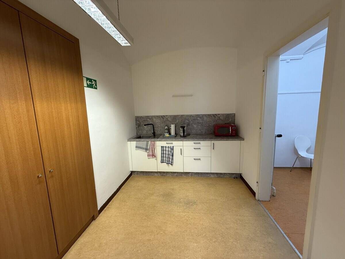 Kleine Küchenzeile mit weißen Schränken, Spüle und Mikrowelle, ergänzt durch einen großen Holzschrank.