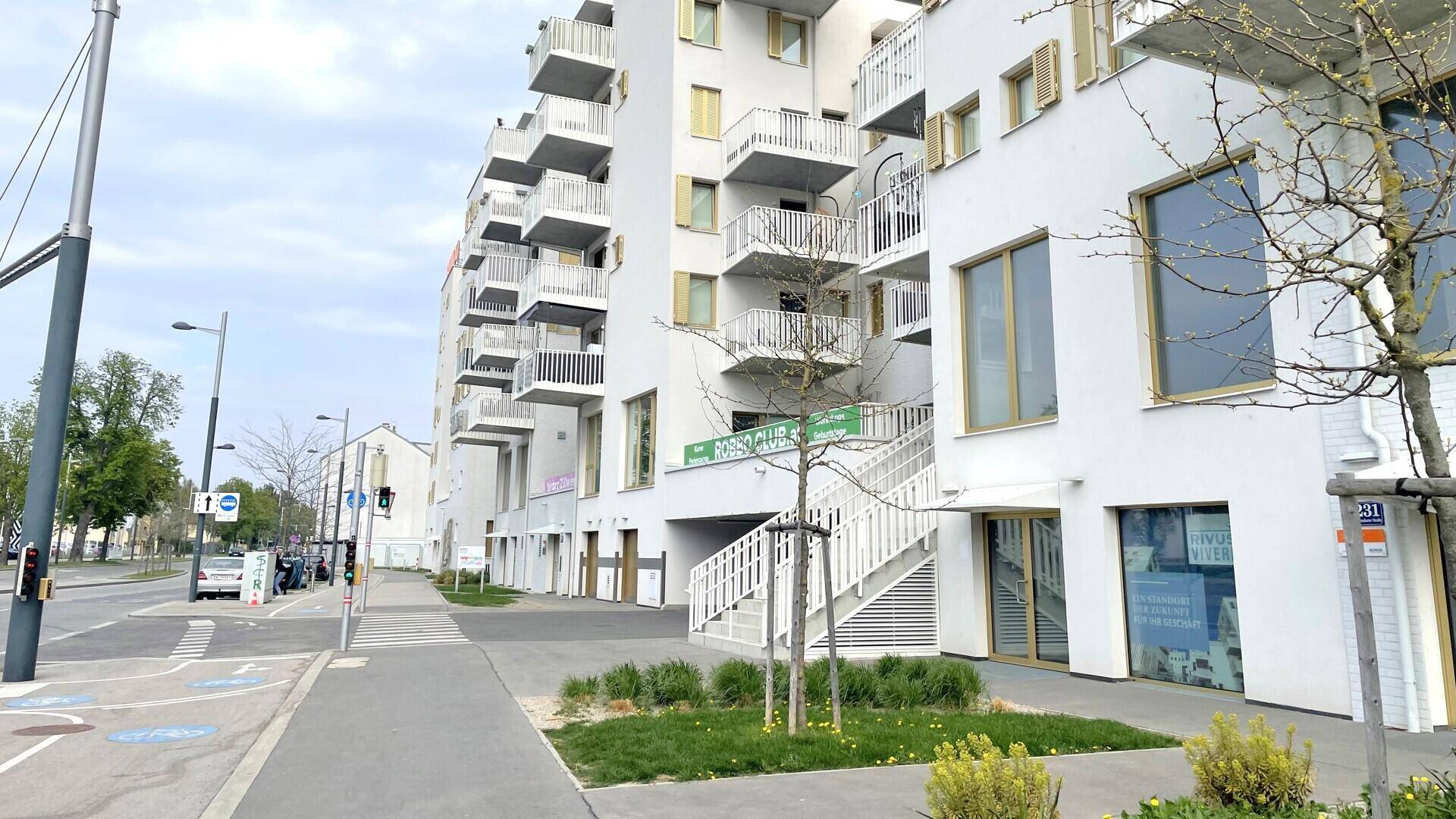 Gesamtansicht des modernen Wohn- und Geschäftsgebäudes entlang einer Straße mit Bäumen und Gehwegen.