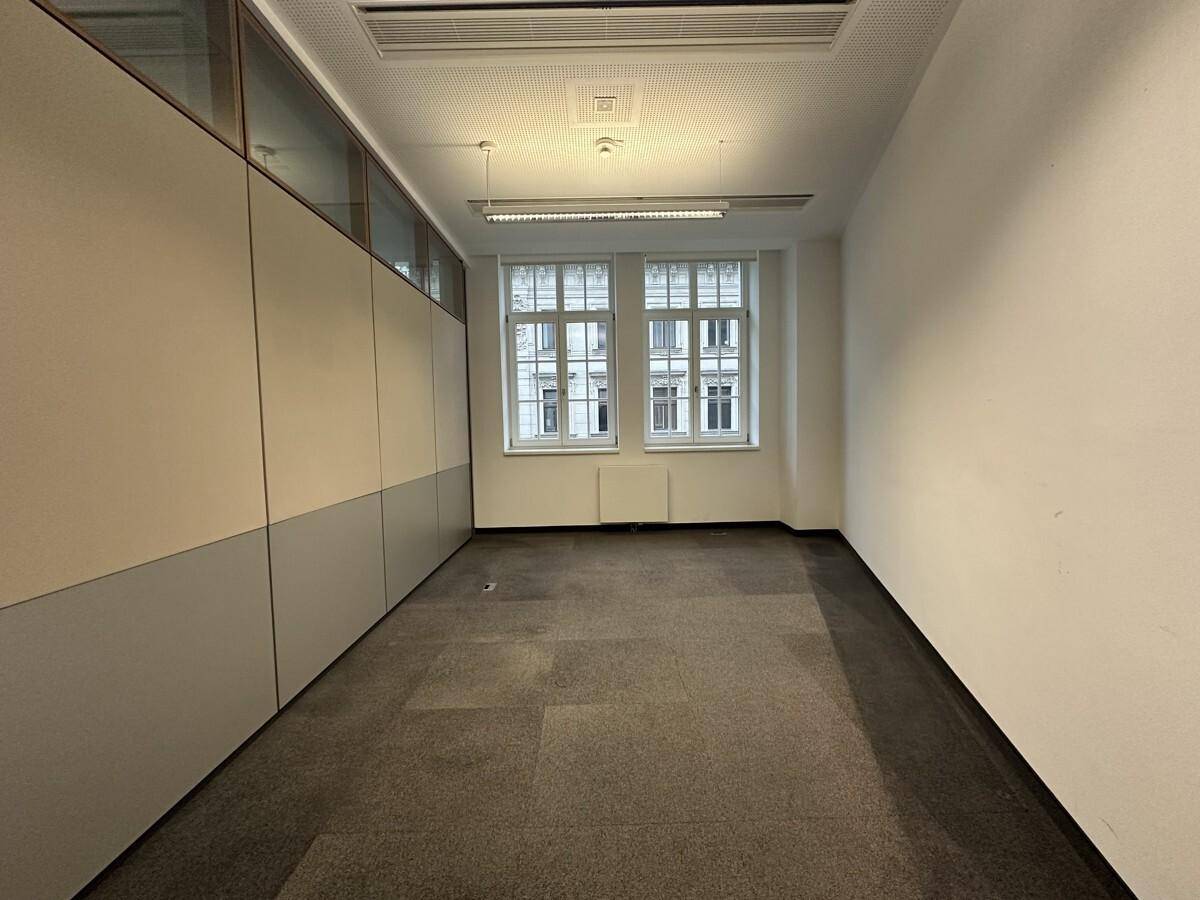 Kleinerer Büroraum mit Teppichboden, zwei Fenstern und integrierten Schränken an der Wand, ideal für Einzelbüros.