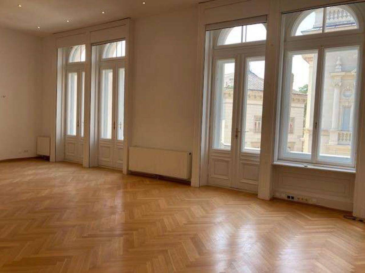 Eleganter Raum mit Fischgrätparkett, hohen Fenstertüren und viel natürlichem Lichteinfall.