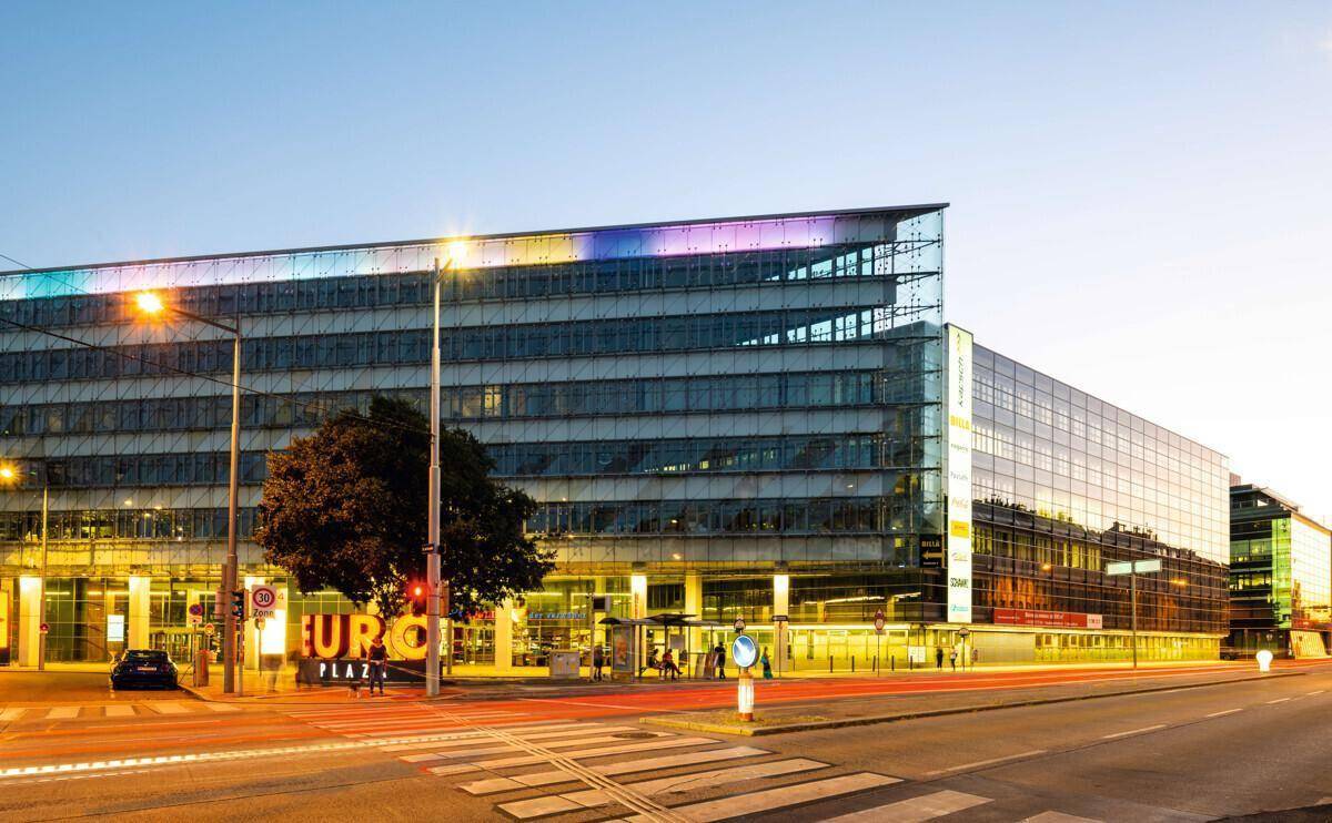Modernes Bürogebäude mit farbiger Beleuchtung und beleuchtetem "EURO PLAZA" Schriftzug bei Dämmerung.
