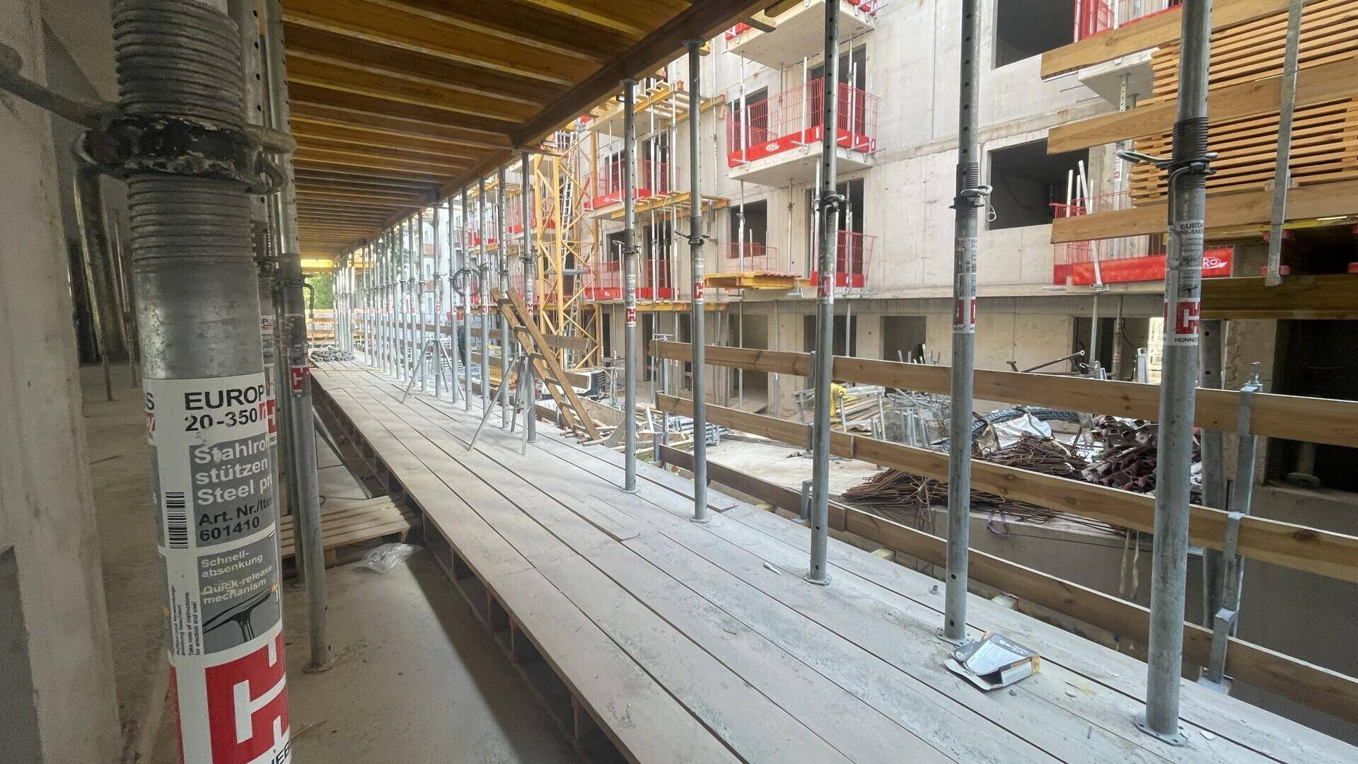 Blick entlang eines Baugerüsts mit Holzplanken und Metallstützen an der Fassade eines Neubaus.