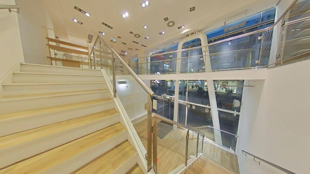 Elegante Treppe mit Glasgeländer und Holzstufen, die den hellen Verkaufsraum mit dem Obergeschoss verbindet.