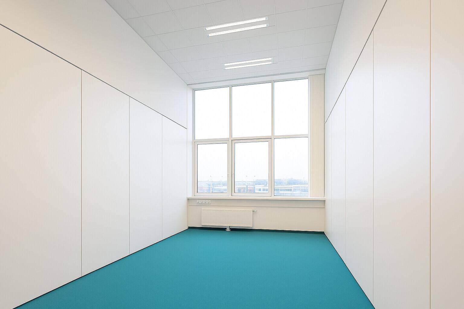 Schmaler Büroraum mit Einbauschränken, großem Fenster und hellem, modernem Design.