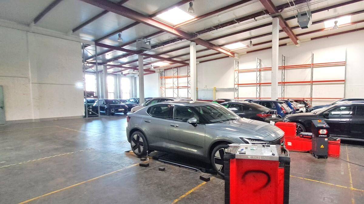 Große Halle mit mehreren Autos, Werkstattausrüstung und hohen Decken, beleuchtet durch Oberlichter.