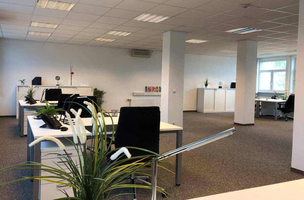 Heller, offener Bürobereich mit mehreren Schreibtischen, Teppichboden und effizienter Deckenbeleuchtung.