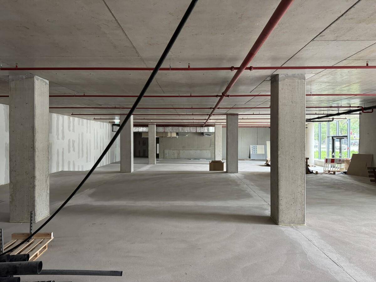 Ein großer, unfertiger Gewerberaum mit Betonboden, Säulen und sichtbaren roten Rohren an der Decke.