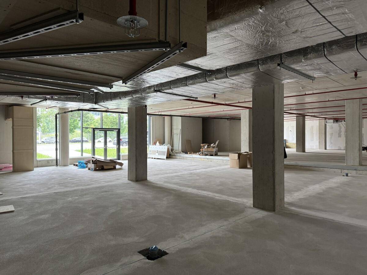 Ein weitläufiger, unfertiger Gewerberaum mit Betonstützen und sichtbaren Installationen an der Decke.
