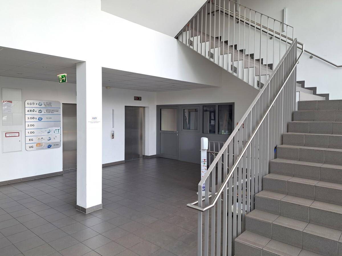 Heller Eingangsbereich mit Treppenhaus, Aufzug und Fliesenboden in einem modernen Geschäftsgebäude.