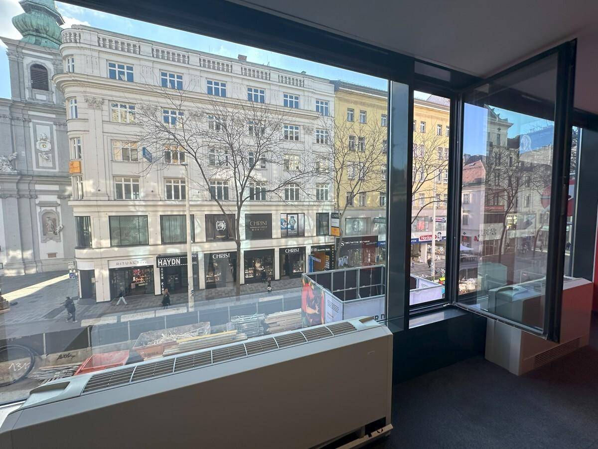 Geräumiger Innenraum mit großen Fenstern und Blick auf die belebte Stadtstraße und historische Gebäude.