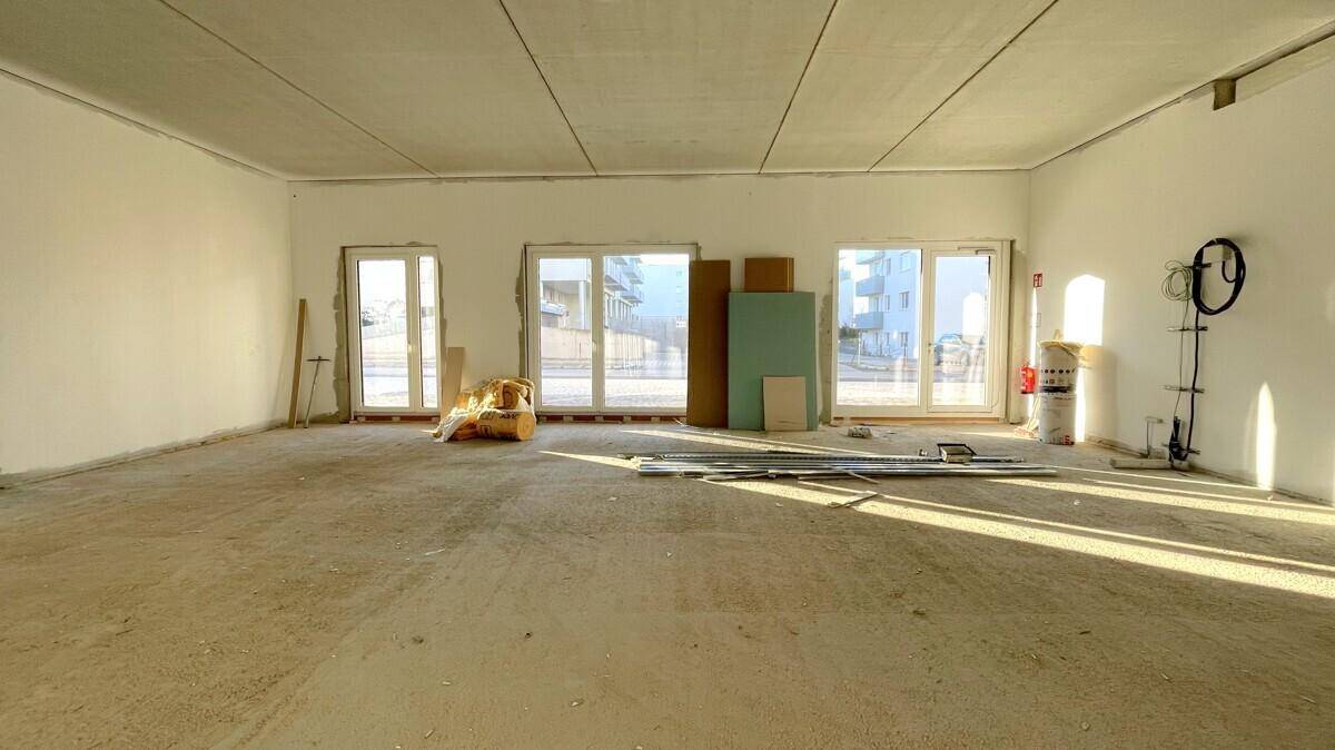 Unfertiger Innenraum mit großen Fensterfronten und Baumaterialien, die auf den Ausbau warten.