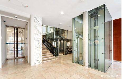 Geräumige Lobby mit mehreren Glasaufzügen, einer Treppe und Marmorakzenten.