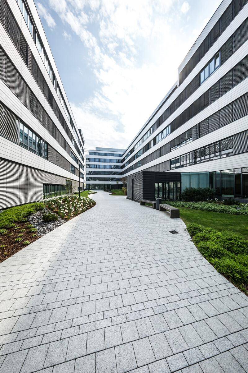 Moderner Bürokomplex mit symmetrischer Architektur, gepflasterten Wegen und grünen Rasenflächen zwischen den Gebäuden.