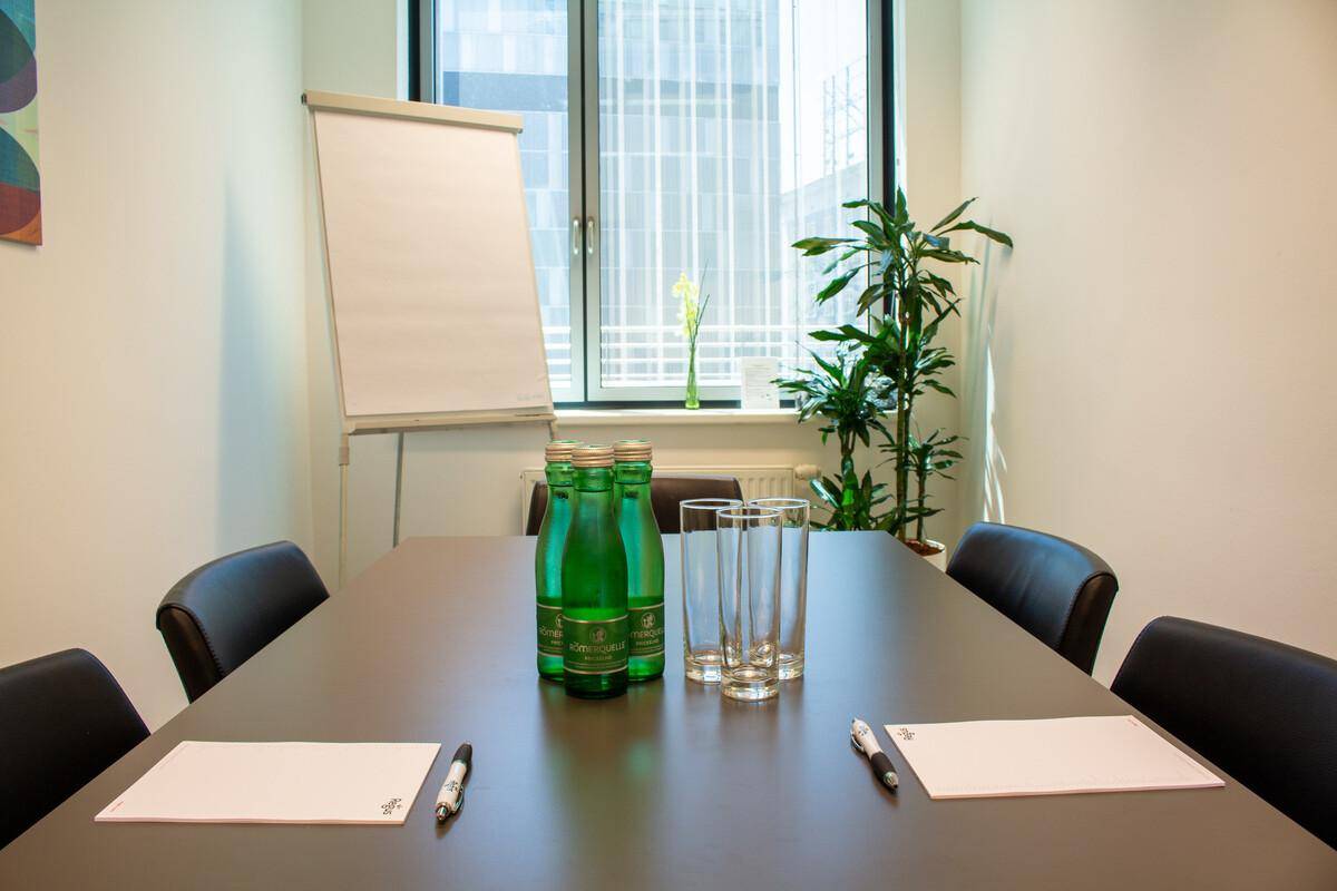 Kleiner Besprechungsraum mit dunklem Tisch, bequemen Stühlen und einem Flipchart, ideal für private Meetings.