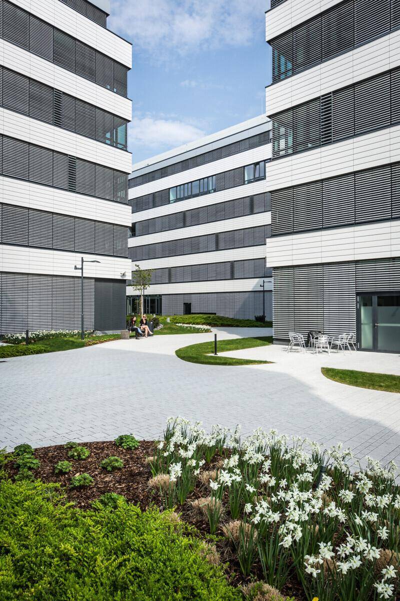 Moderner Bürokomplex mit gepflastertem Innenhof, Grünflächen und Sitzgelegenheiten für entspannte Pausen.