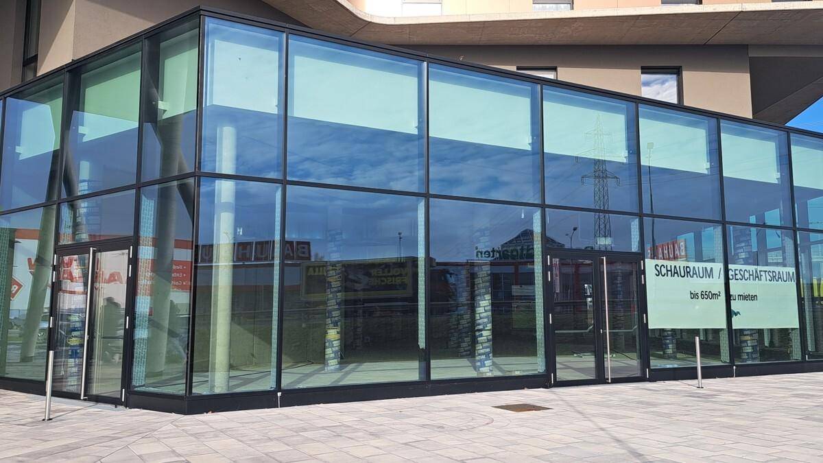 Detaillierte Ansicht der Glasfassade des Erdgeschosses mit reflektierendem Himmel und Hinweisschildern.