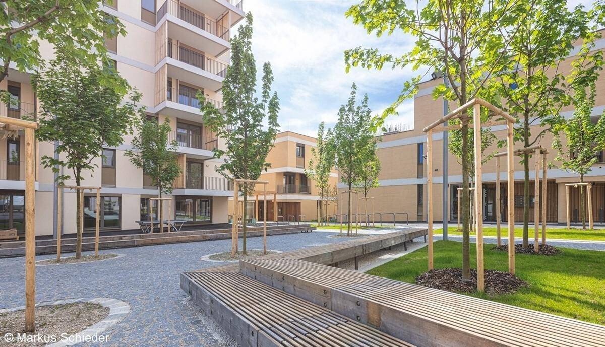 Attraktiver Innenhof einer modernen Wohnanlage mit Sitzgelegenheiten, Bäumen und gepflasterten Wegen.