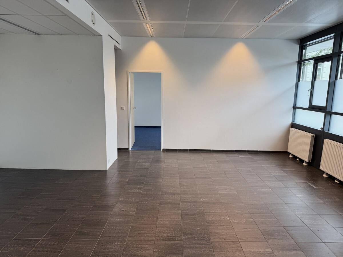 Geräumiger, leerer Büroraum mit großen Fenstern, Fliesenboden und Zugang zu weiteren Räumen.