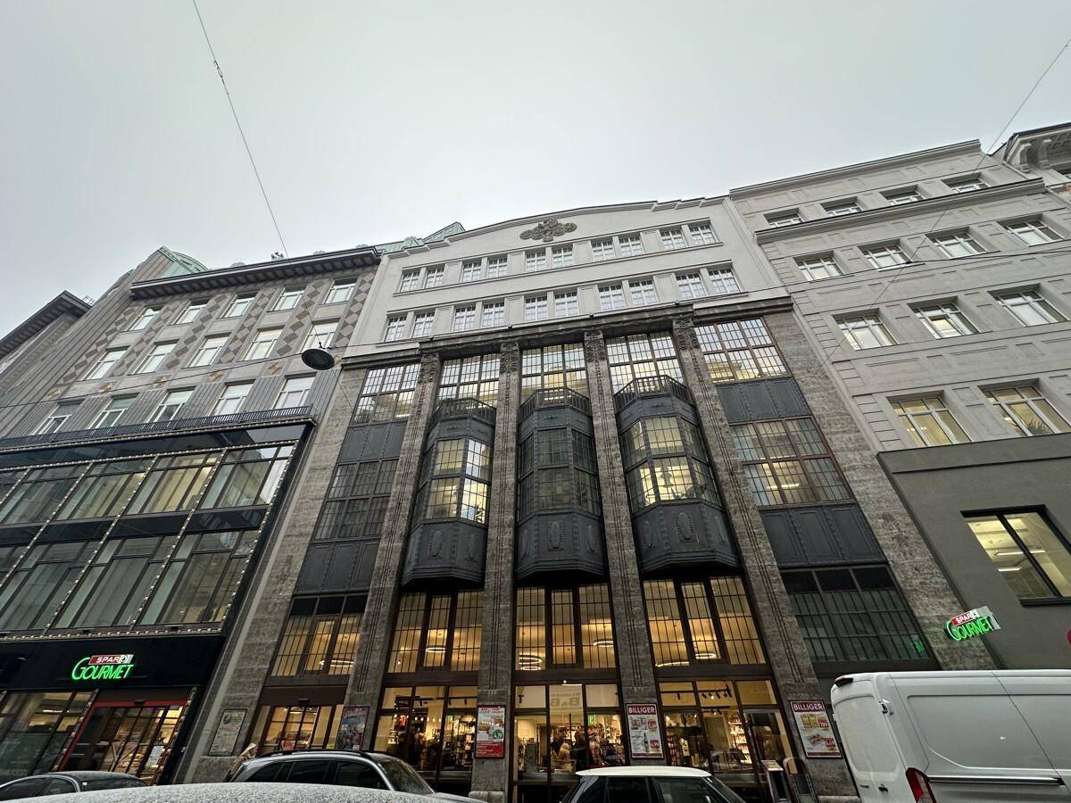 Gesamtansicht der beeindruckenden Gebäudefassade mit Geschäften im Erdgeschoss und vielen Fenstern in der Stadt.