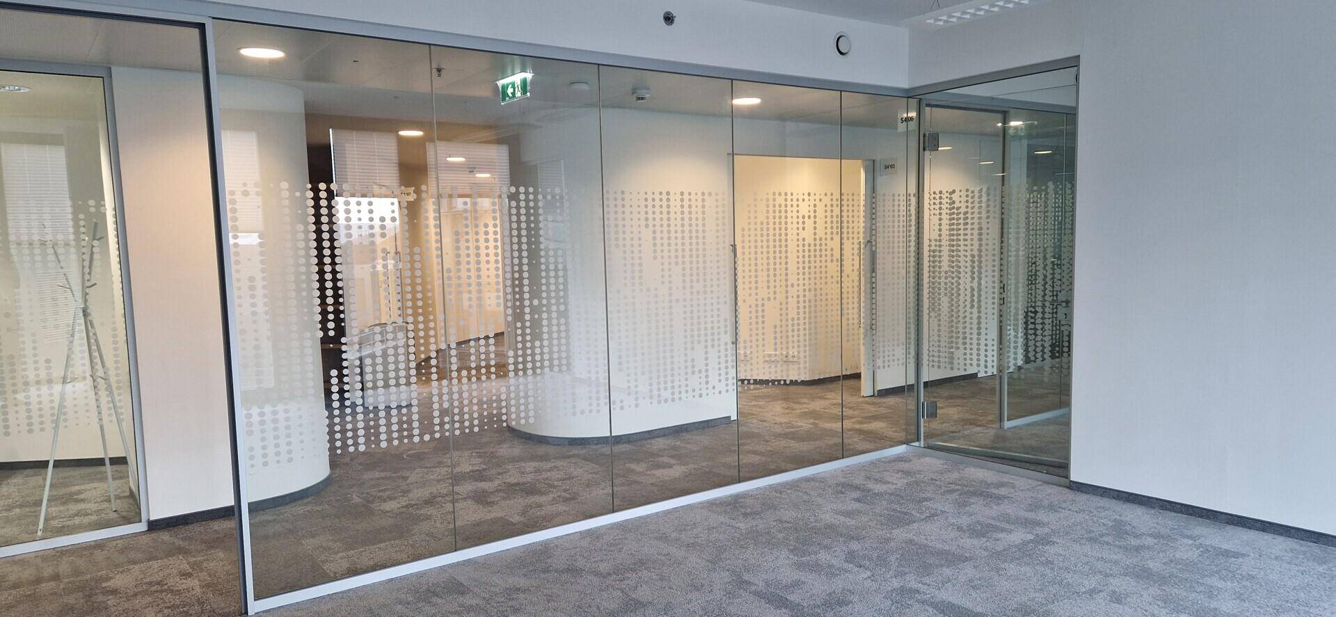 Moderner Bürogang mit Glaswänden und dezentem Punktmuster, der zu weiteren Büroräumen führt.