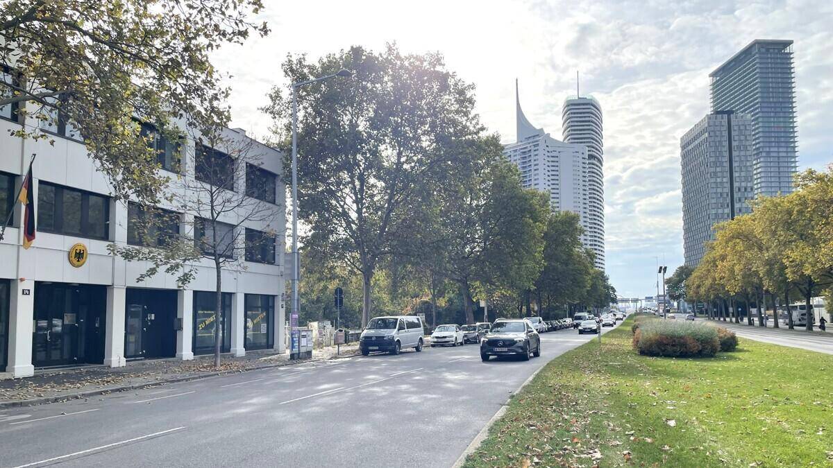 Blick auf das Geschäftsgebäude mit der Straße, Bäumen und modernen Hochhäusern im Hintergrund.