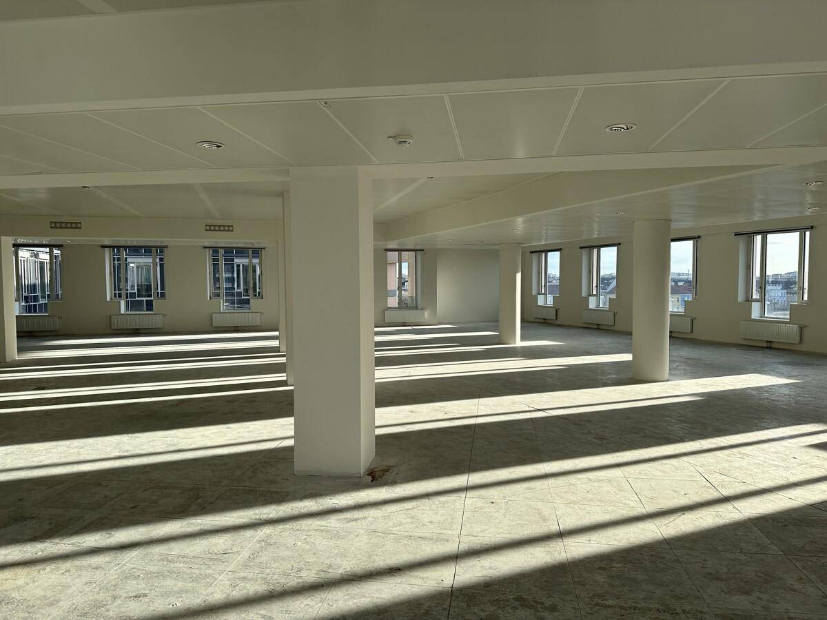 Geräumiger Bürobereich mit vielen Fenstern, tragenden Säulen und einem Boden aus Beton und Fliesen.