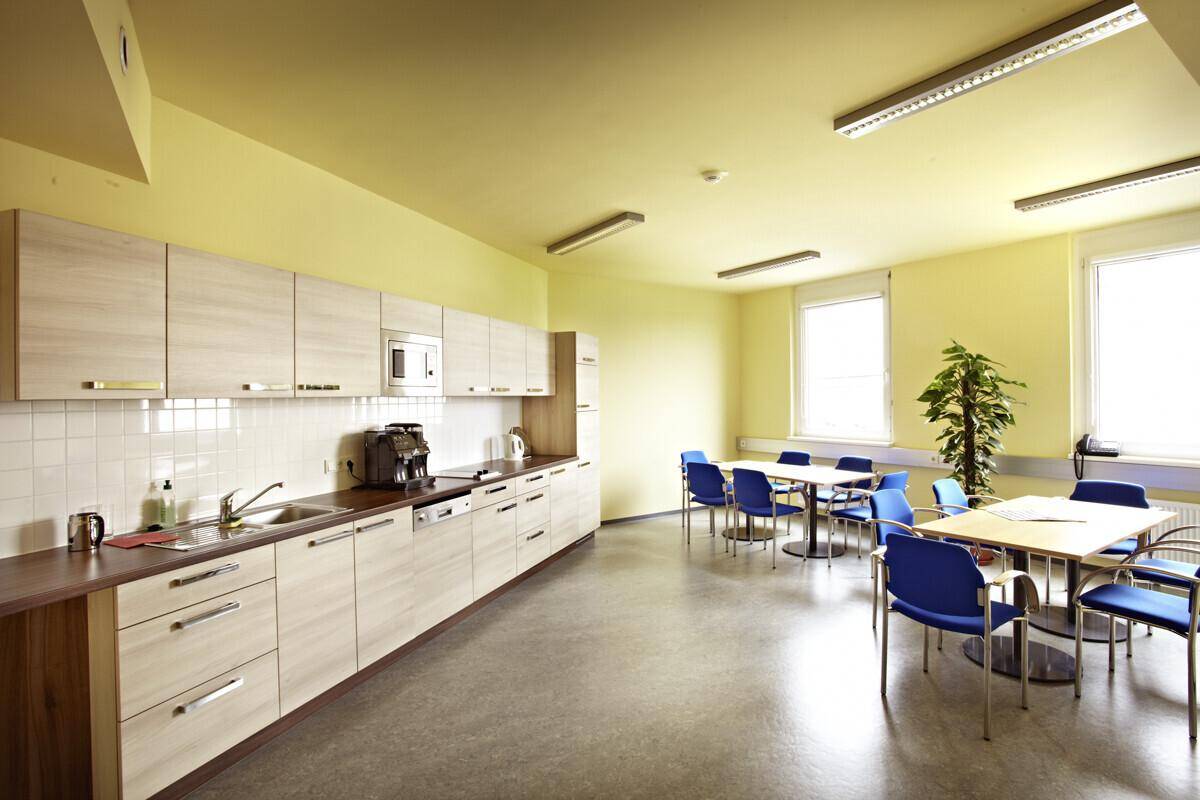 Moderne Teeküche oder Pausenraum mit Einbauküche, Esstischen und blauen Stühlen in einem Büro.