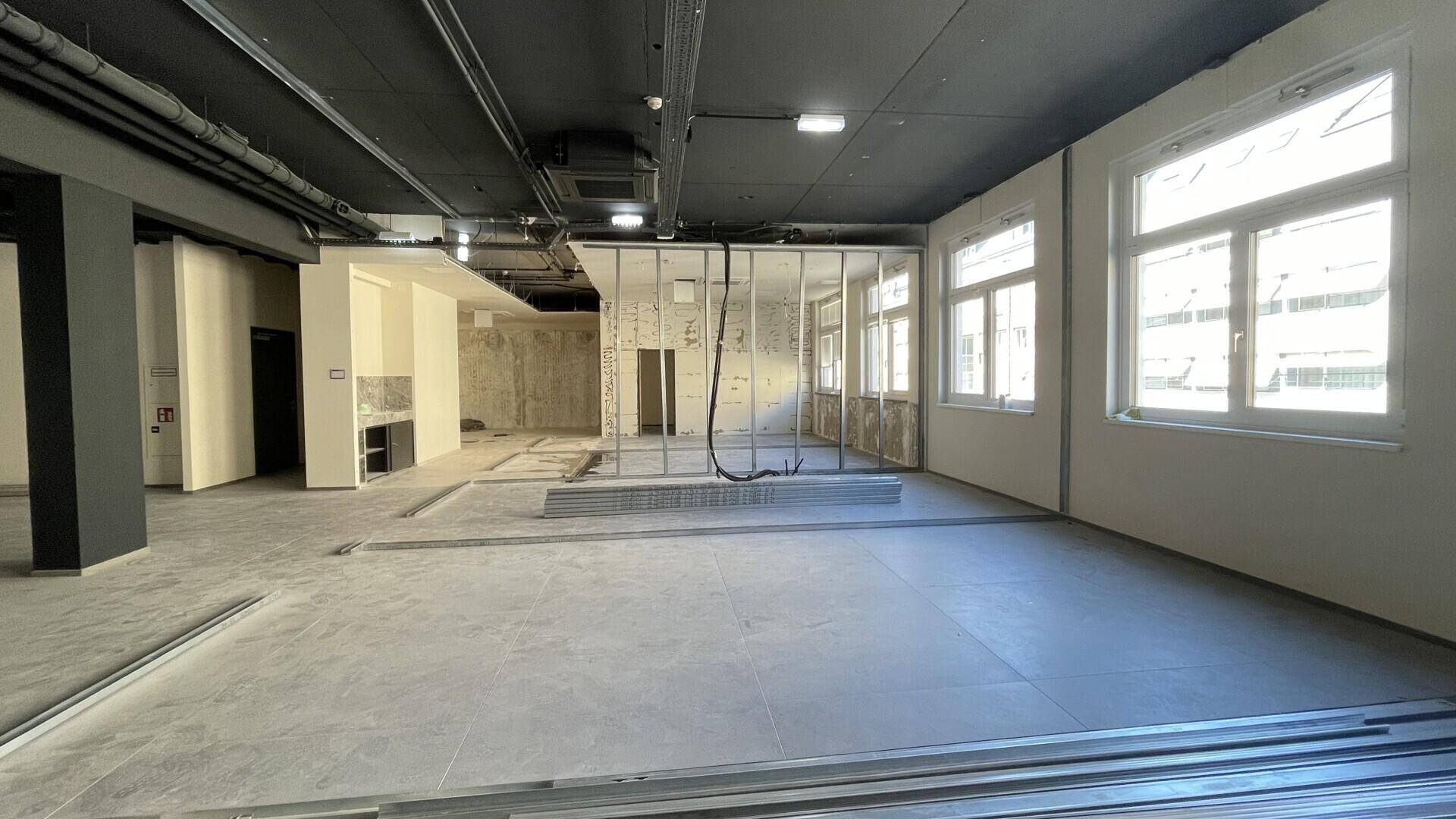 Großer, heller Büroraum im Rohbau mit vielen Fenstern und Betonboden.