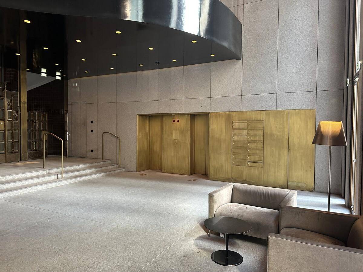 Elegante Lobby mit goldfarbenen Aufzugstüren, Steinboden und bequemen Sitzgelegenheiten in einem modernen Gebäude.