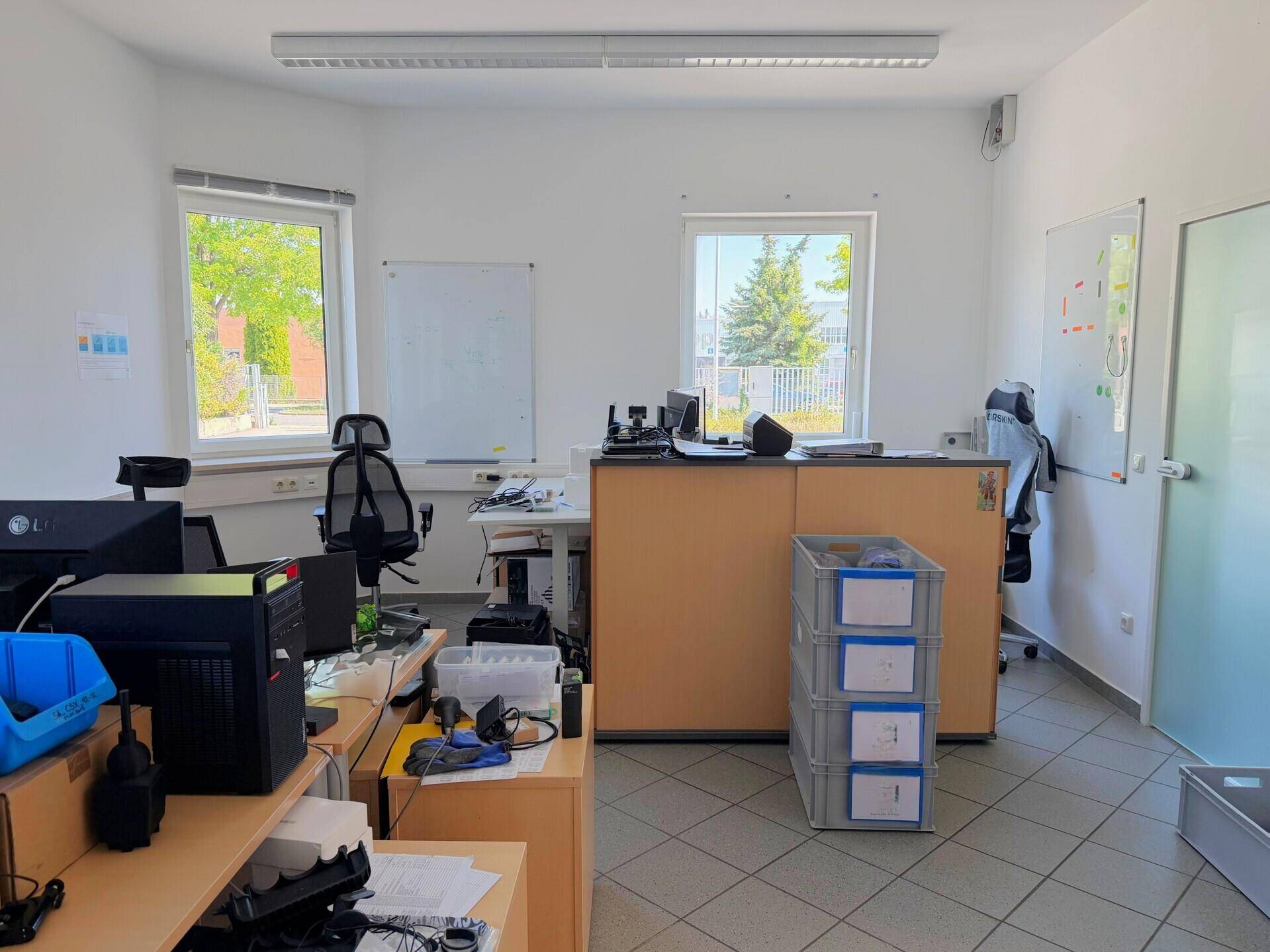 Helles Büro mit mehreren Arbeitsplätzen, Bürostühlen und Fenstern, die Tageslicht hereinlassen.