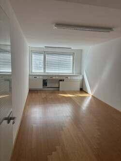 Ein langer, schmaler Büroraum mit Holzboden, einem Fenster und integrierten Unterschränken entlang der Wand.