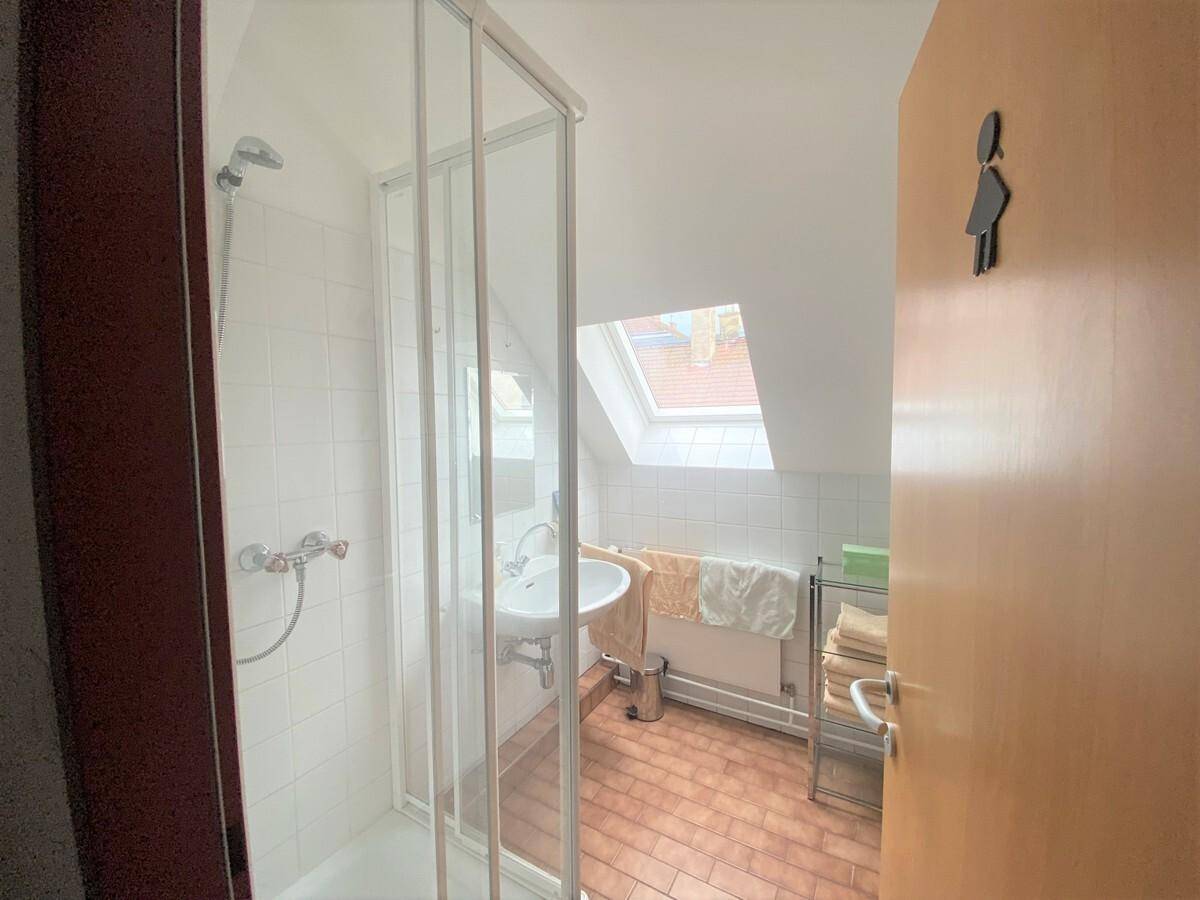 Kleines Badezimmer im Dachgeschoss mit Duschkabine, Waschbecken und einem Dachfenster.