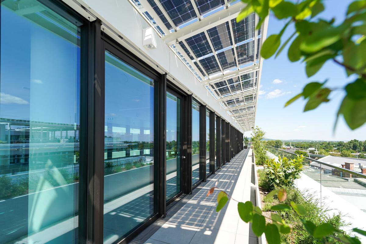Lange Terrasse im Obergeschoss mit Solarpaneelen als Überdachung und weitem Blick über die Umgebung.