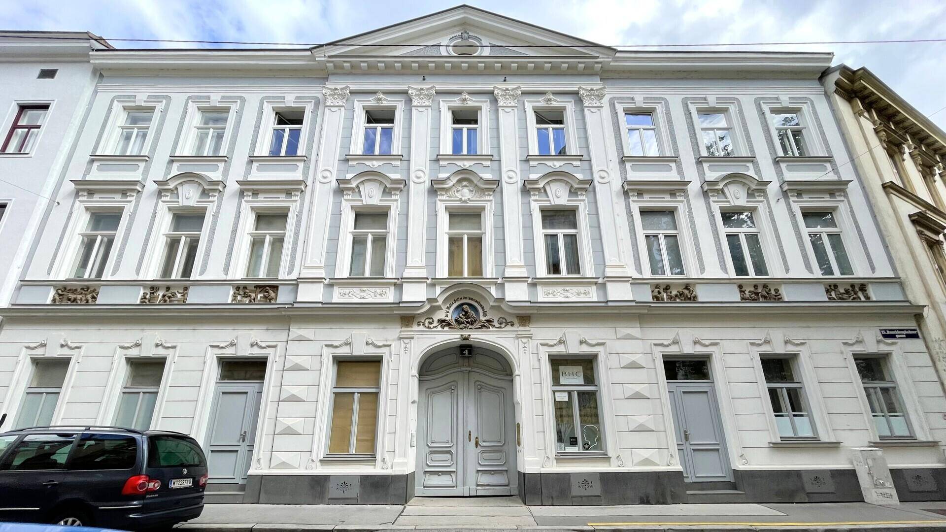 Historisches Gebäude mit reich verzierter Fassade und großen Fenstern an einer Stadtstraße.