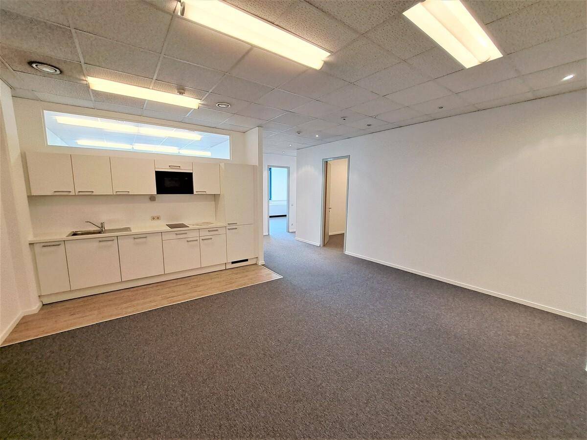Großes Büro mit integrierter Küchenzeile, Teppichboden und Zugang zu weiteren Räumen.