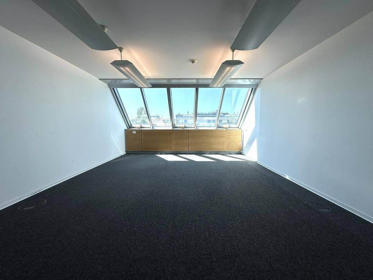 Helles Büro mit Teppichboden, schrägen Wänden und breiter Fensterfront im Dachgeschoss.
